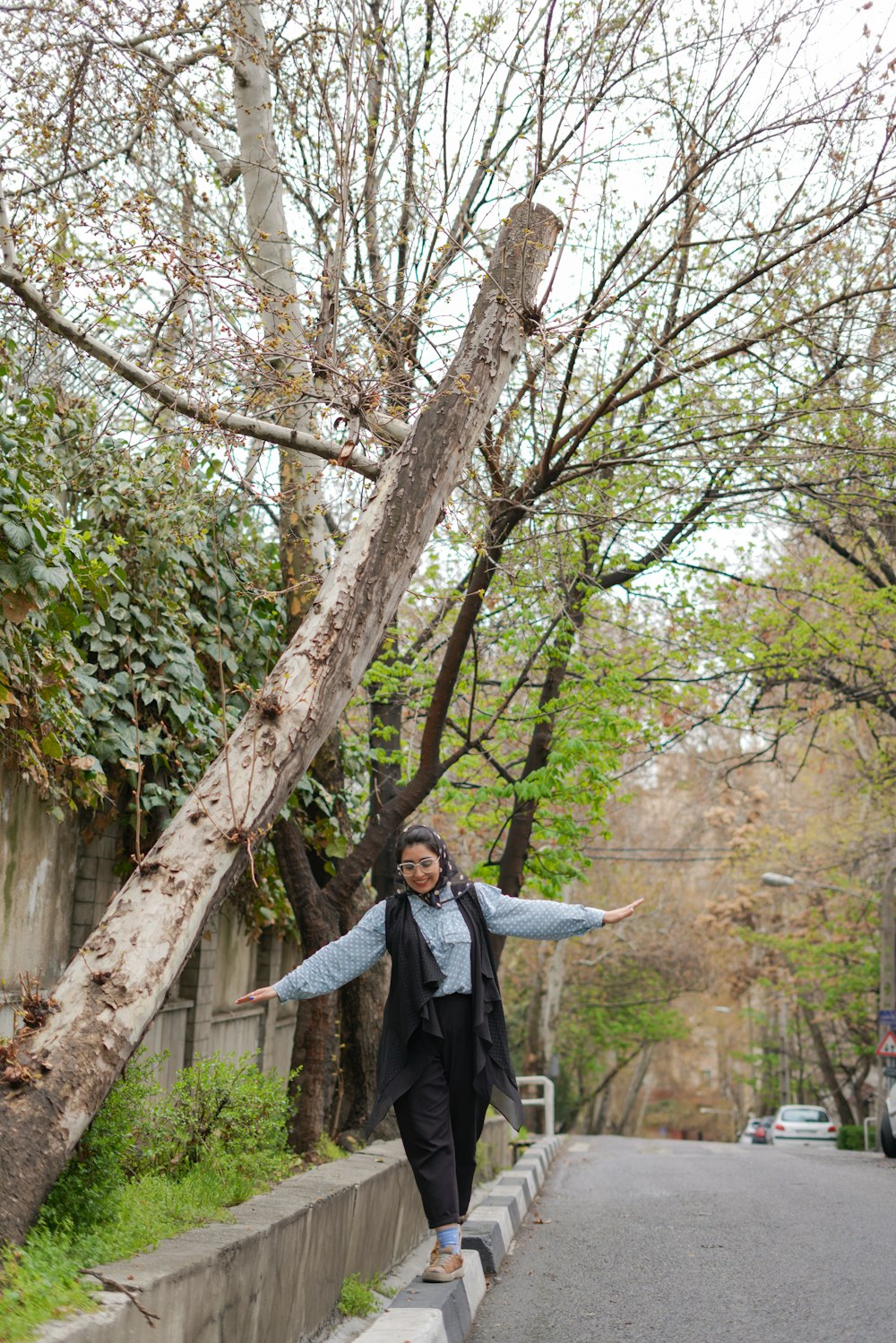 a woman walking down a street next to a tree