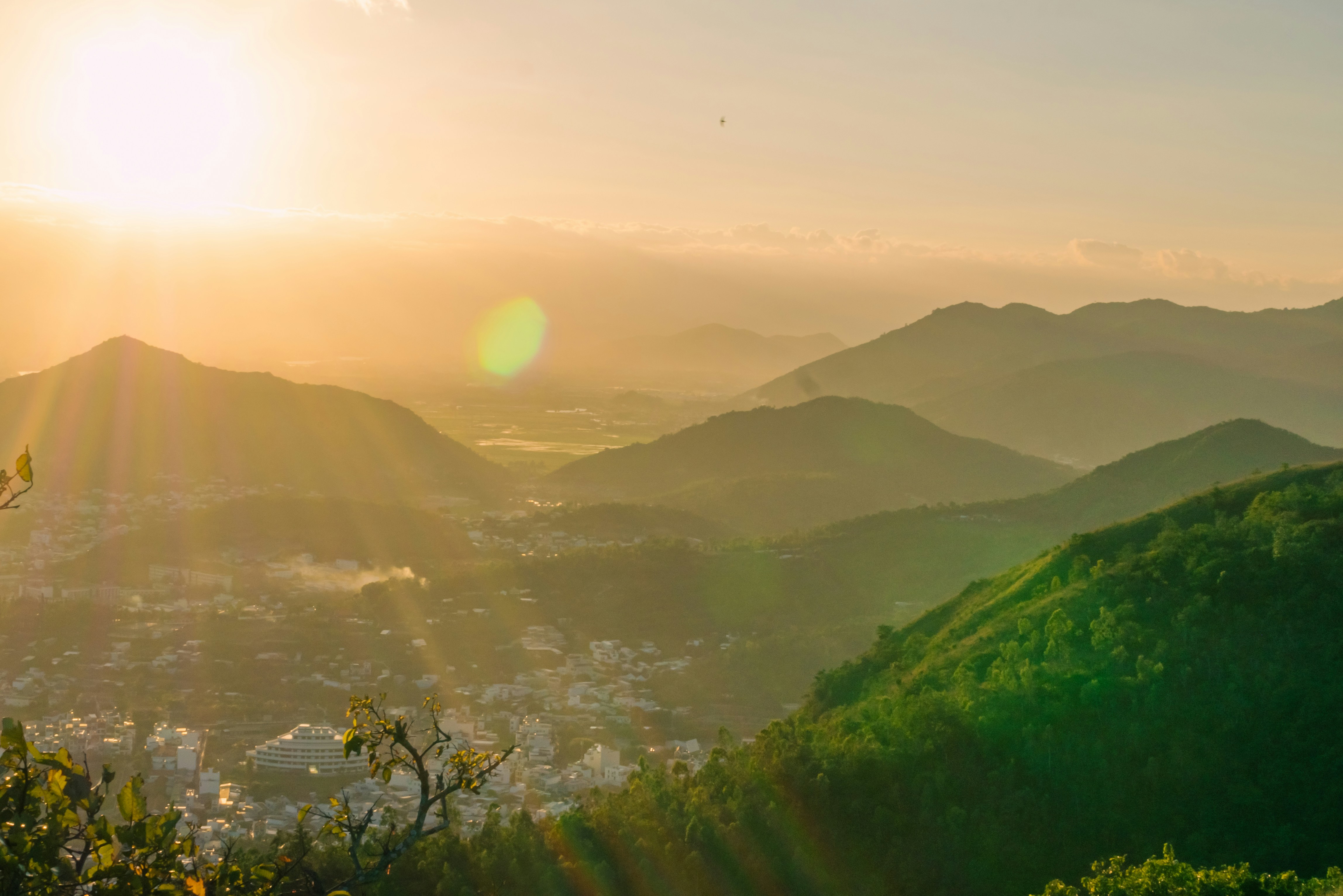 the sun is setting over a city and mountains