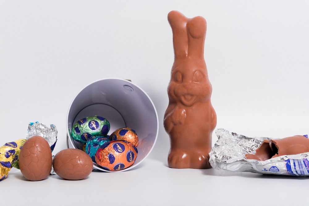 a chocolate bunny sitting next to a bucket of chocolate eggs