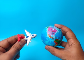 Hand holding earth globe and airplane on blue background.