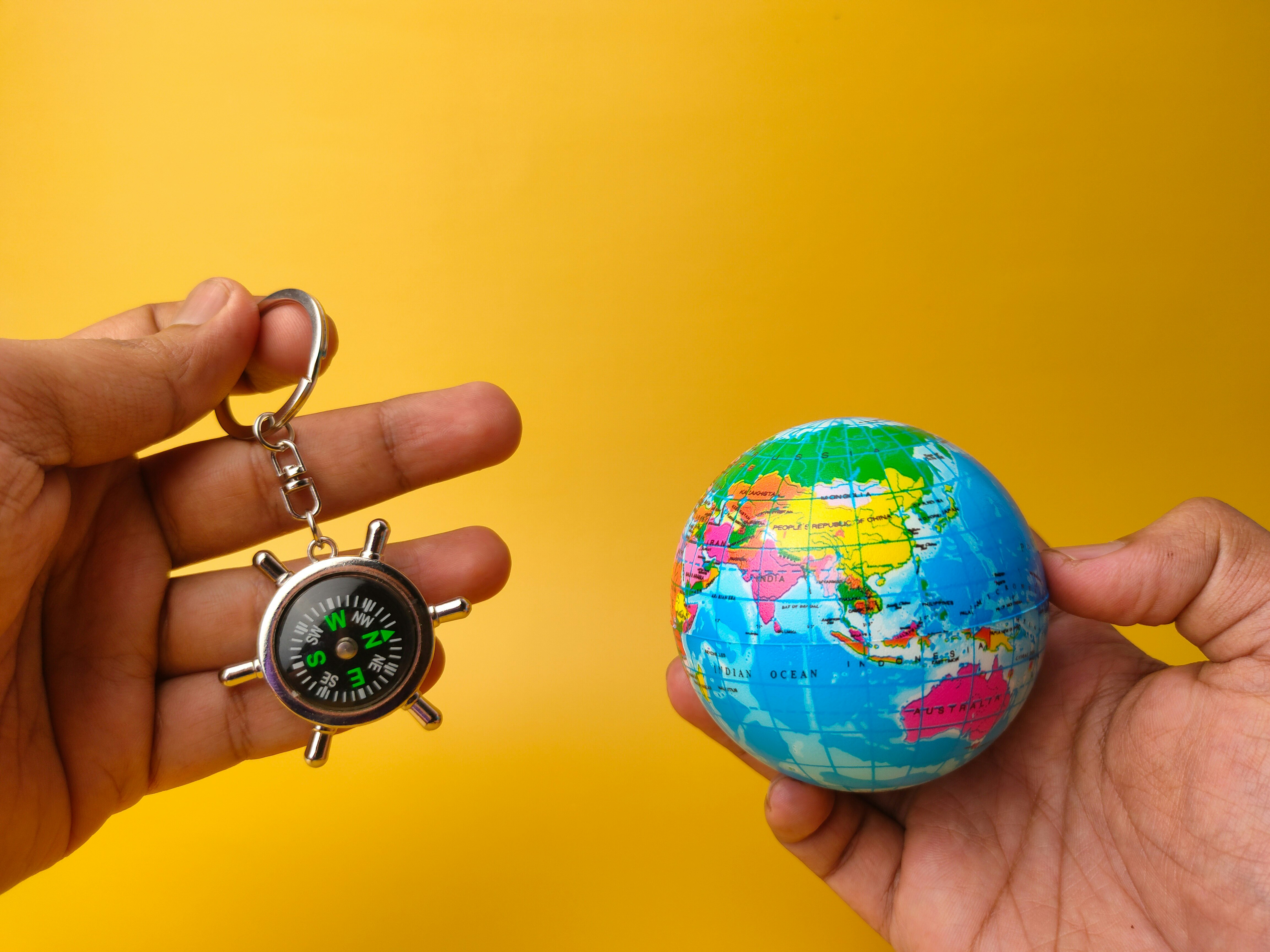 Hand holding earth globe and compass on yellow background.