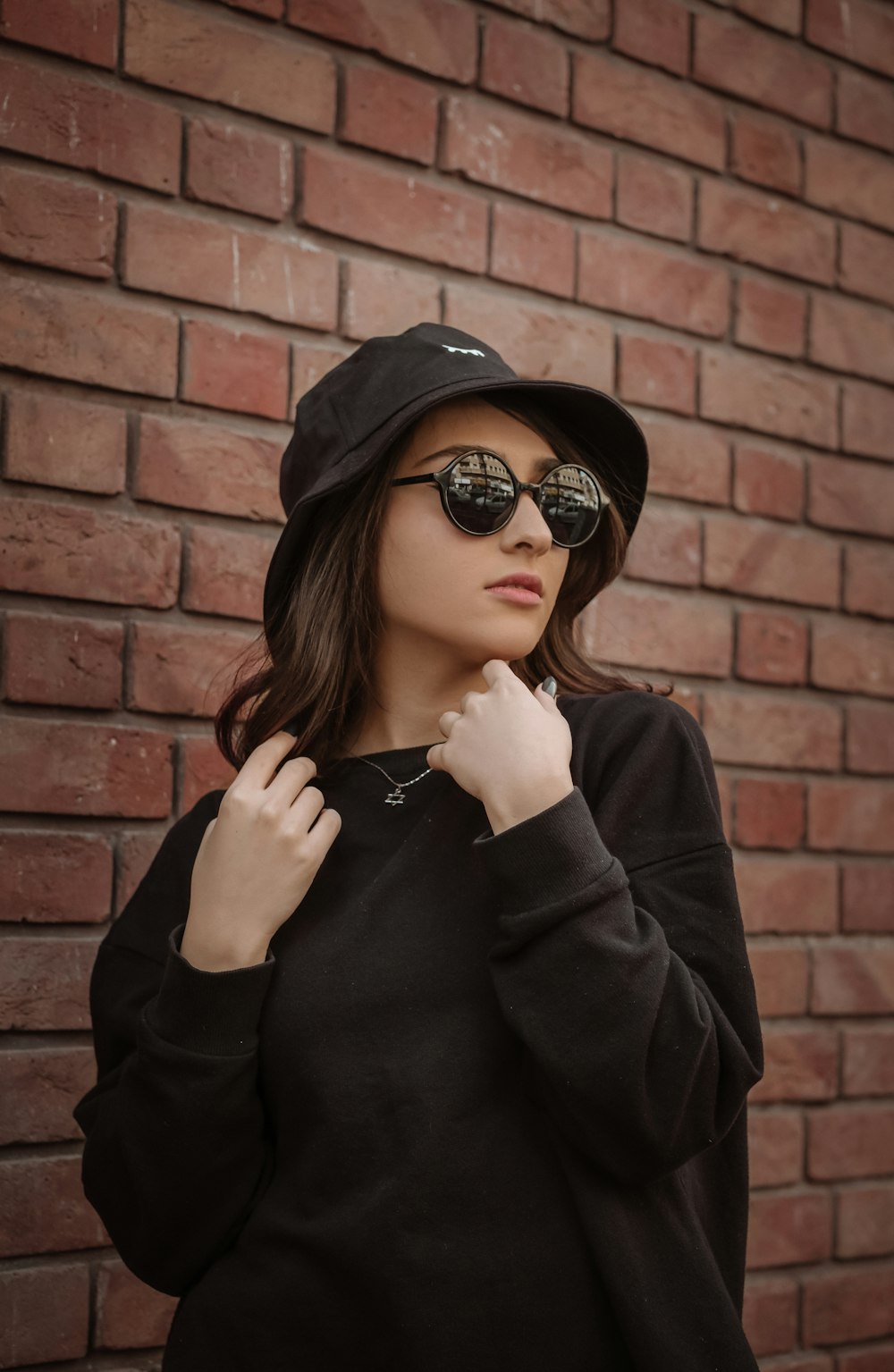 a woman wearing a hat and sunglasses standing in front of a brick wall