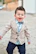 Smiling toddler dressed in elegant, handmade children's clothing outdoors.