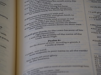 A close-up of an open book showing printed text, with emphasis on a passage from a psalm. The pages appear to be slightly aged, with the text clearly legible and organized in verses.