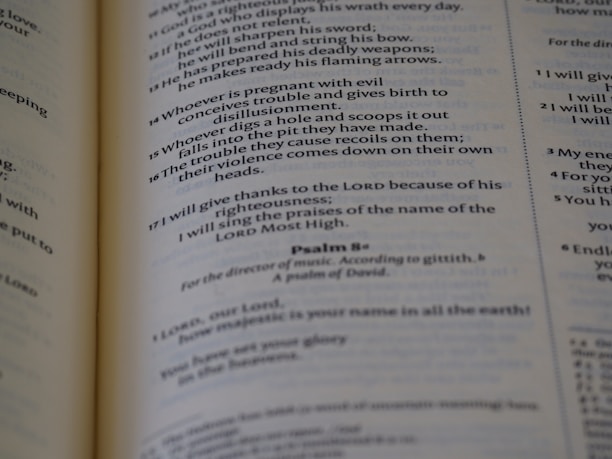 A close-up of an open book showing printed text, with emphasis on a passage from a psalm. The pages appear to be slightly aged, with the text clearly legible and organized in verses.