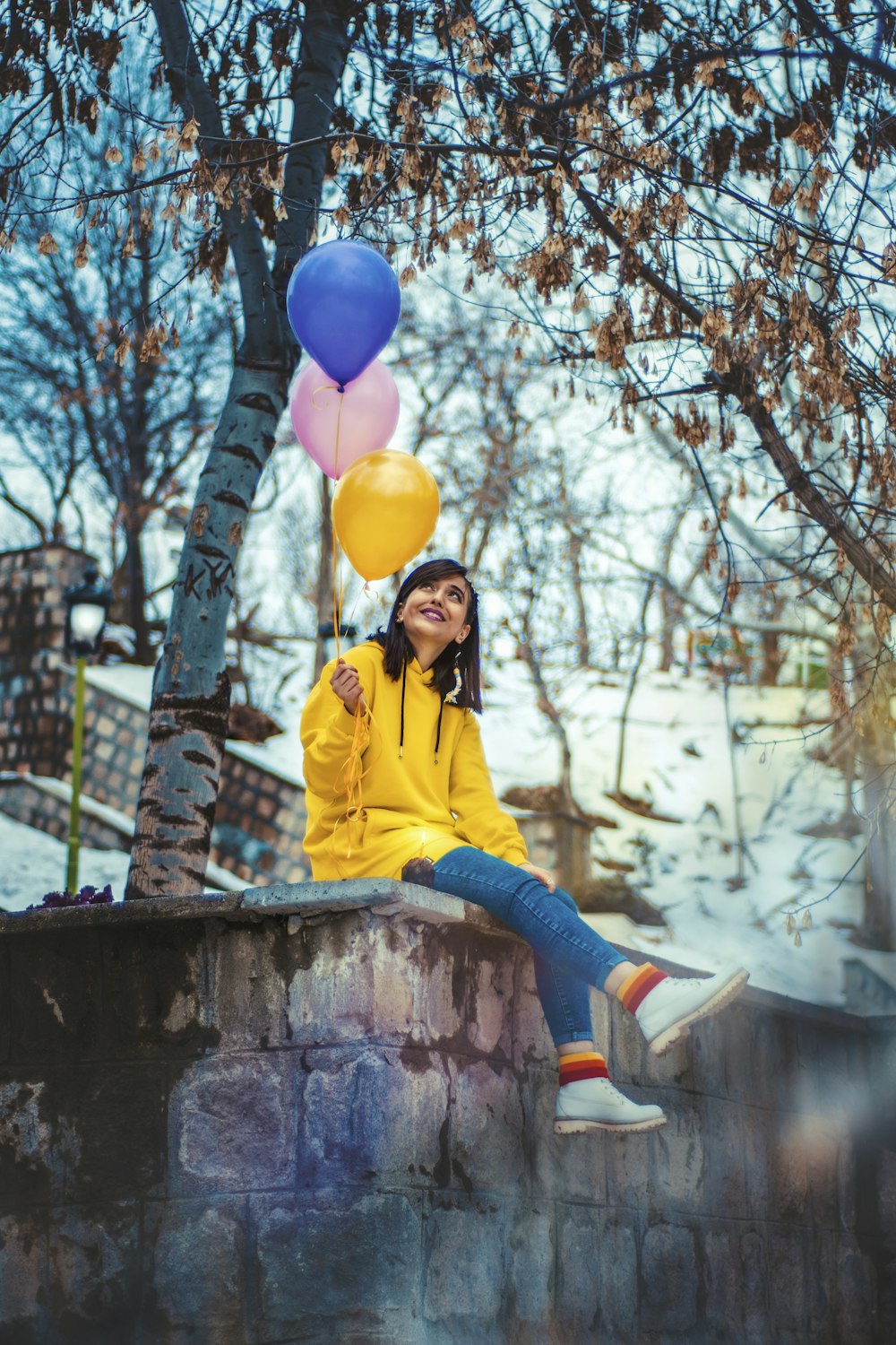 a woman in a yellow jacket sitting on a wall with balloons