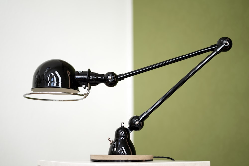 a black lamp on a white table next to a green wall