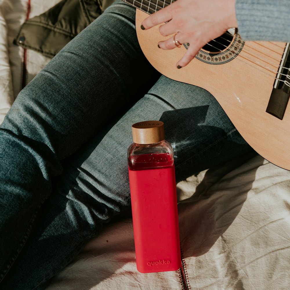 a person sitting on a bed with a guitar and a bottle