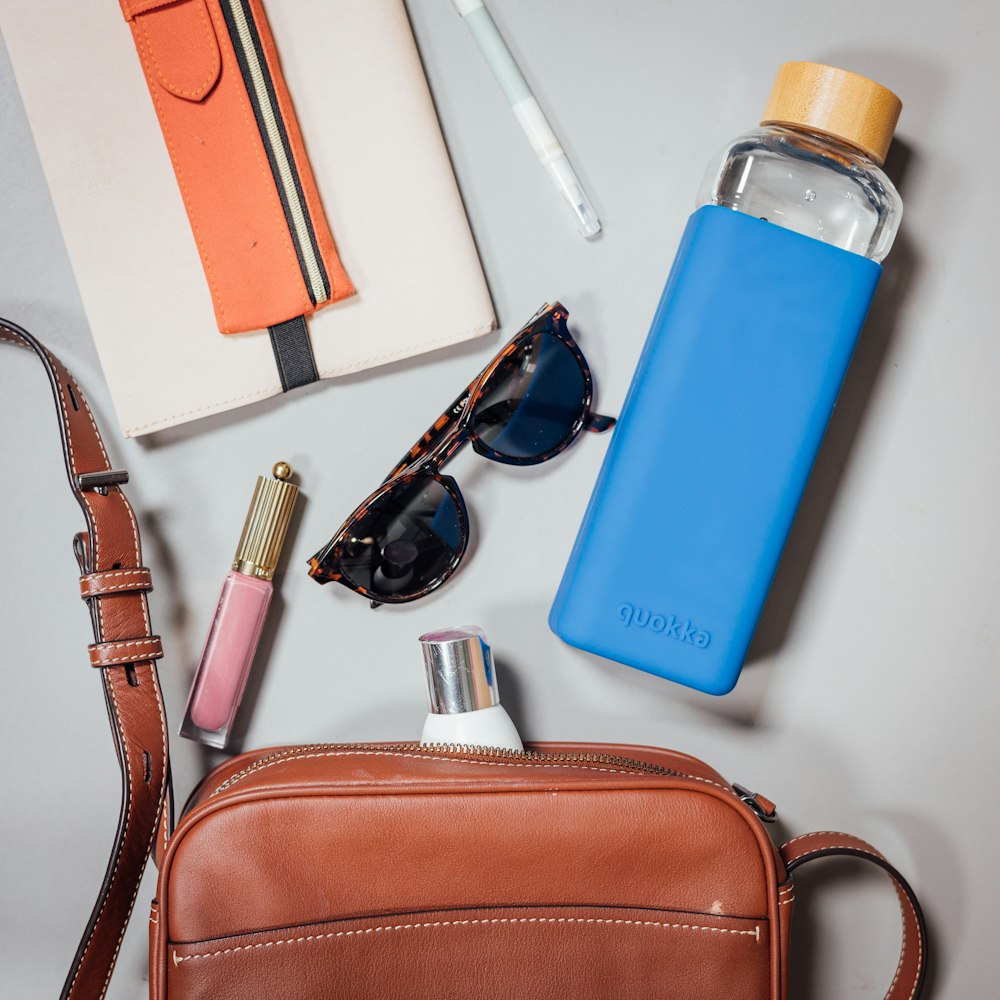 a purse, sunglasses, lipstick, and other items are laid out on a table