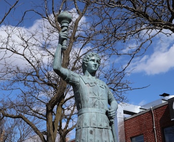 a statue of a man holding a lamp in front of a tree