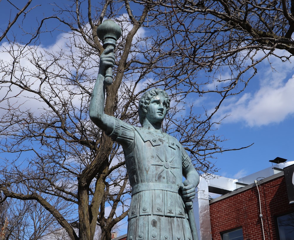 a statue of a man holding a lamp in front of a tree
