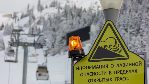 Snow-covered mountain slope with avalanche warning signs and a rescue team in action.