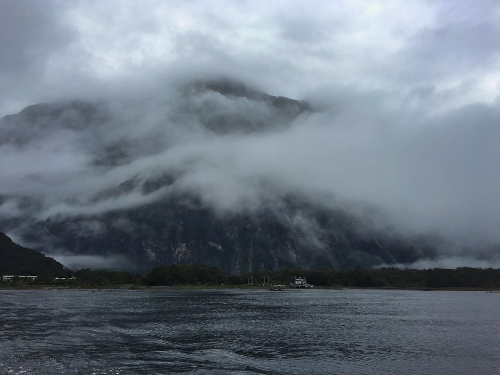 a large mountain covered in clouds next to a body of water