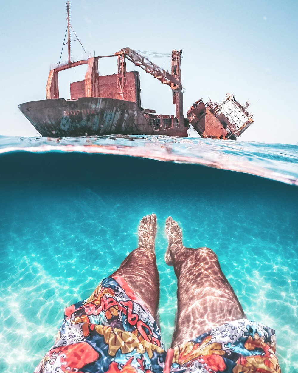 a person's legs in the water with a boat in the background