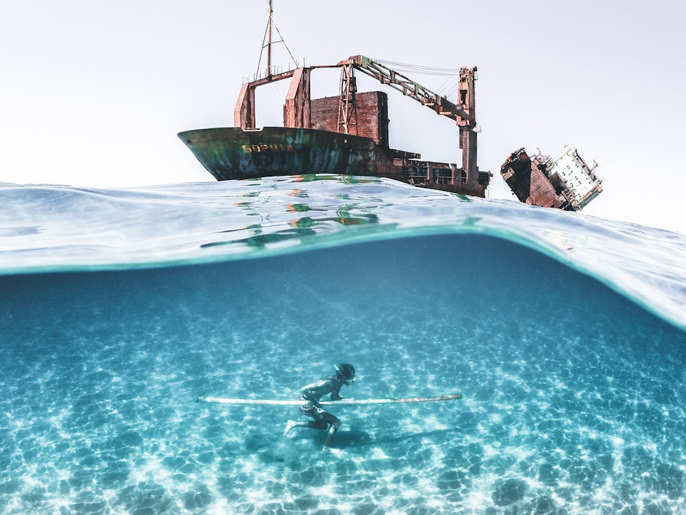 Un hombre montando una tabla de surf debajo de un bote en el océano