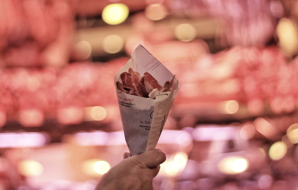 a person holding up a paper cone filled with food