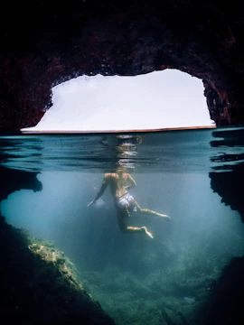 A diver illuminated by a beam of light inside a serene underwater cave surrounded by rugged rock walls.