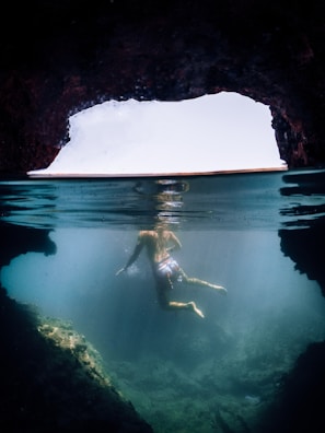 Diver exploring a rocky underwater cave illuminated by natural light