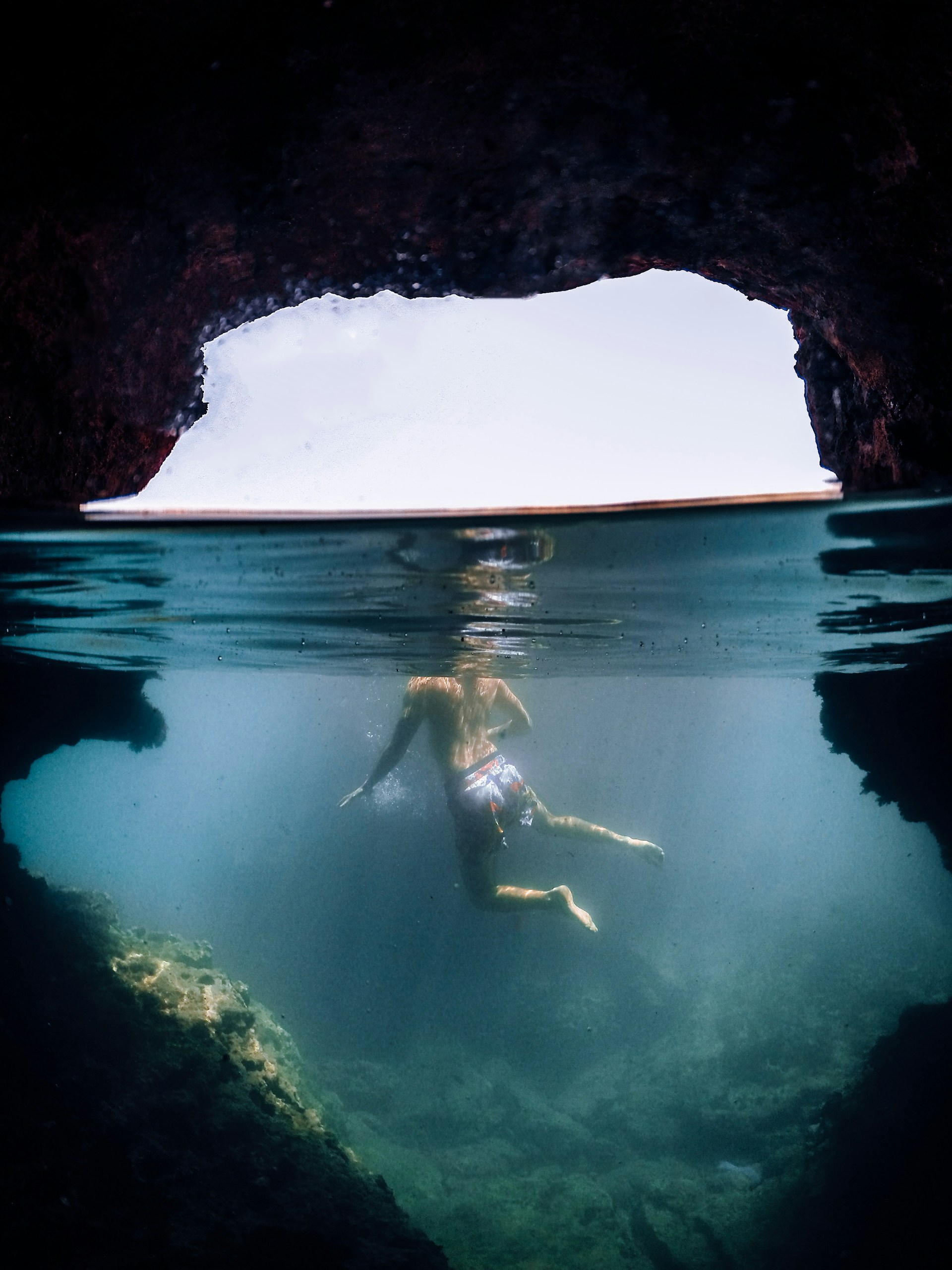 A certified diver exploring an underwater cave, surrounded by shimmering rays of sunlight filtering through the water.