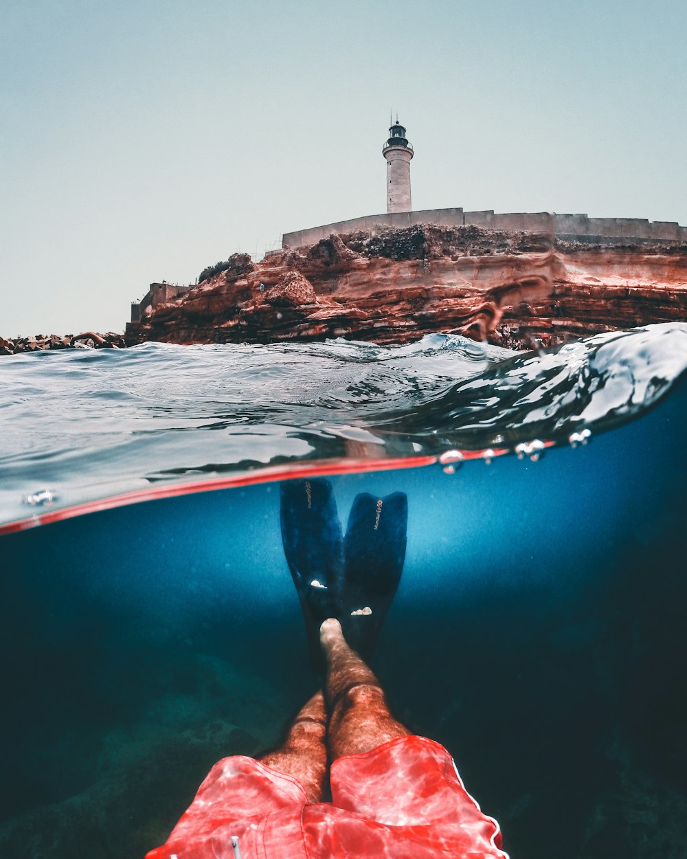 a person's feet in the water with a lighthouse in the background