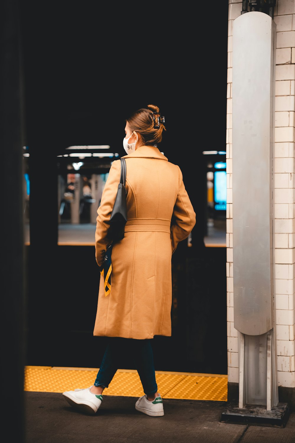 a woman in a tan coat is standing on a subway platform