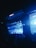 A large outdoor concert stage illuminated with blue lights, featuring a musician or performer in front of a cheering crowd. The stage has an expansive display screen showing graphics and the audience is visible in silhouette.