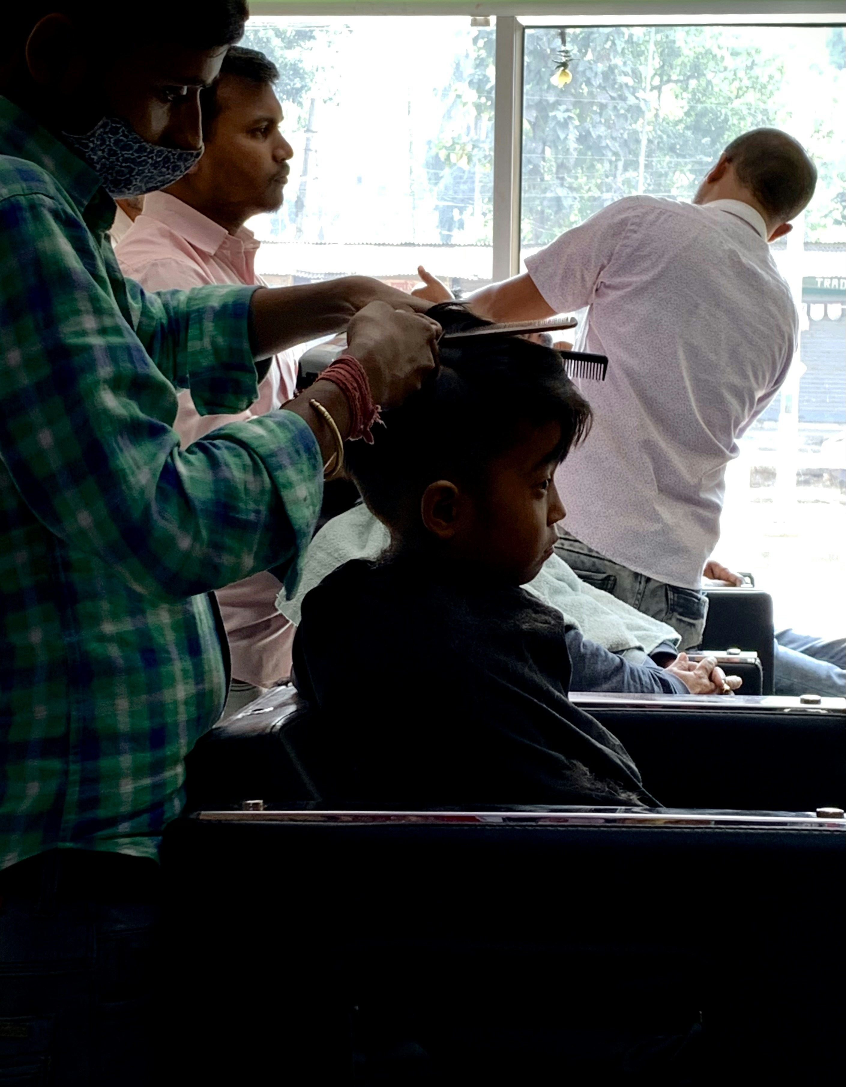 Barber cutting young boys hair, friendly bright barbershop