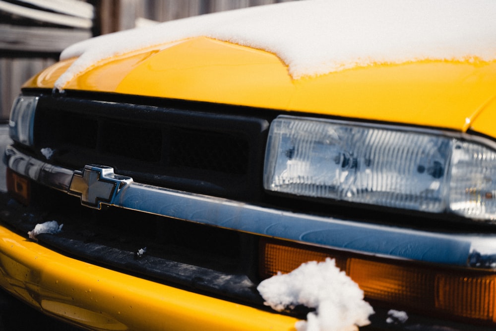 the front of a yellow car covered in snow