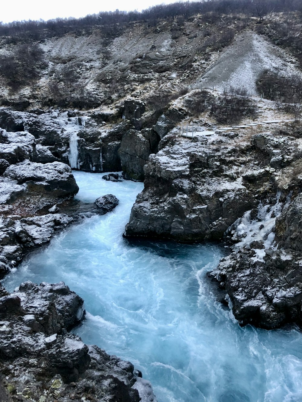 a river running through a rocky hillside covered in snow