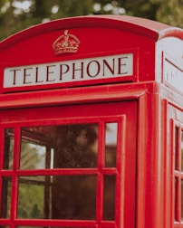 A classic red British telephone booth with glass panels and a sign reading 'TELEPHONE' at the top.