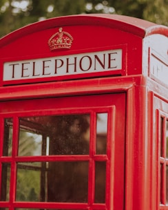 A classic red British telephone booth with glass panels and a sign reading 'TELEPHONE' at the top.