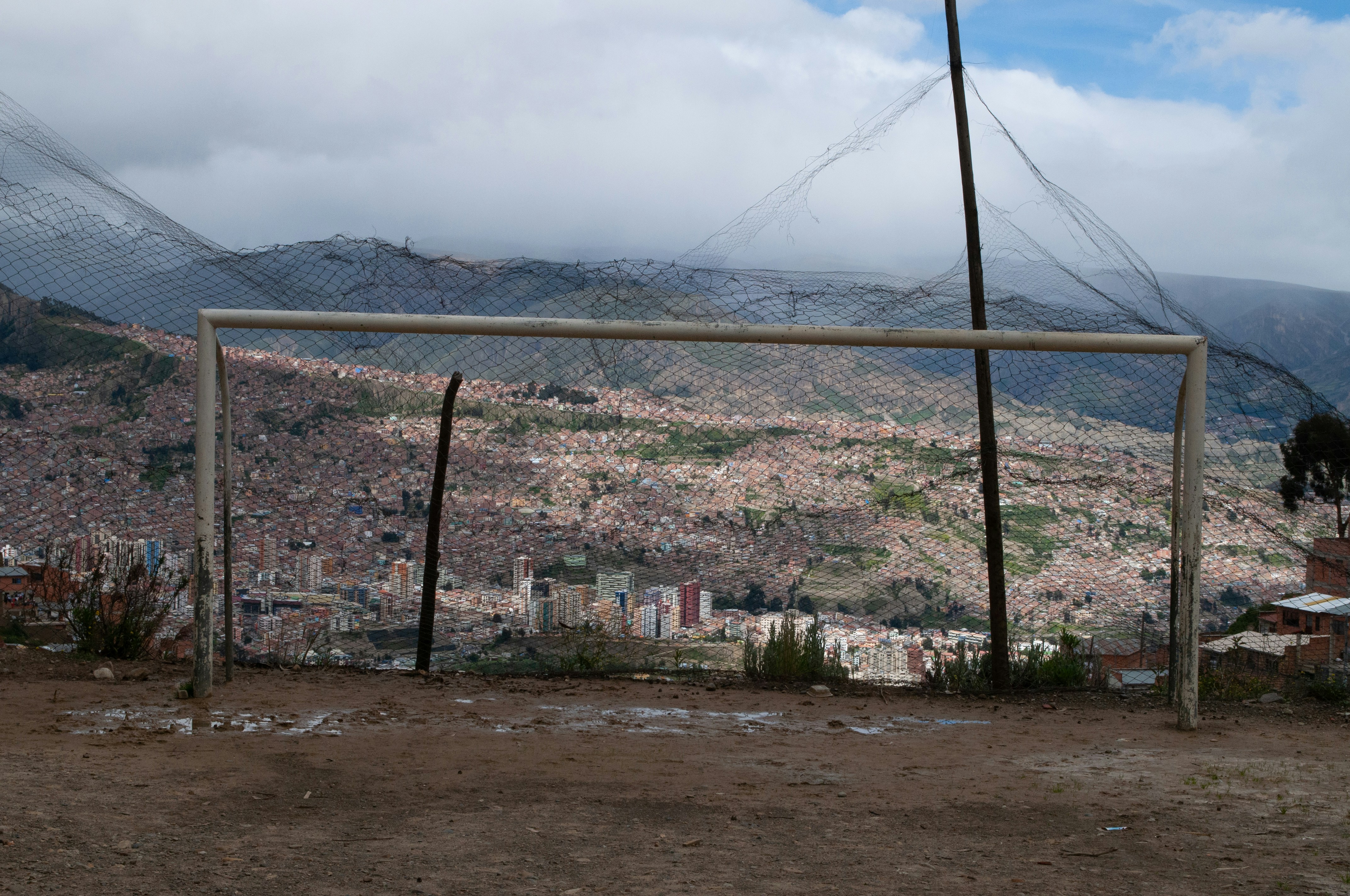 a soccer goal on a dirt field with a city in the background