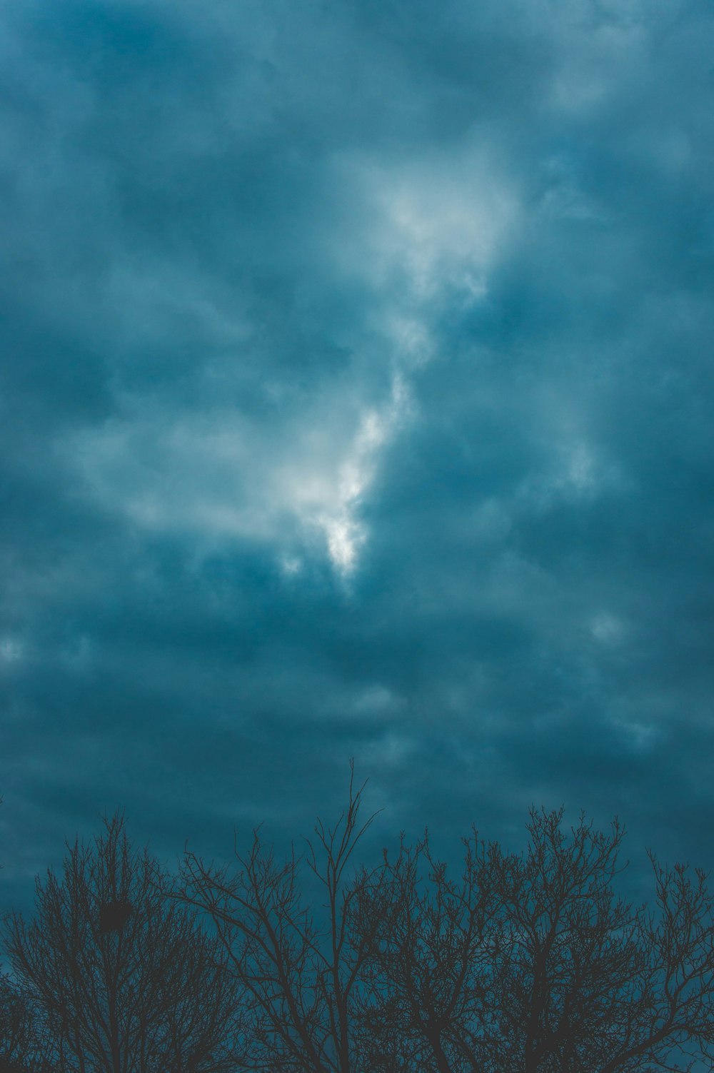 a cloudy sky with some trees in the foreground