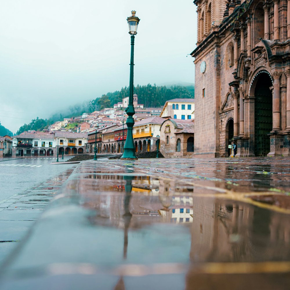 a wet street with a lamp post and buildings in the background