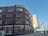 A multi-story brick building with numerous windows, featuring the name 'JACOBS AND CO CARDIFF' at the top. Another building, the 'Clayton Hotel,' stands in the background with a modern design. The street in front has a few parked vehicles, and a railway bridge is visible to the right.