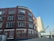 A multi-story brick building with numerous windows, featuring the name 'JACOBS AND CO CARDIFF' at the top. Another building, the 'Clayton Hotel,' stands in the background with a modern design. The street in front has a few parked vehicles, and a railway bridge is visible to the right.