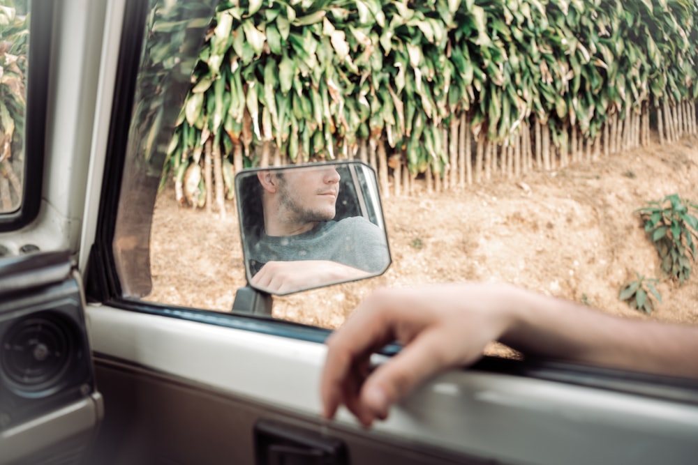 a man's reflection in the side view mirror of a car