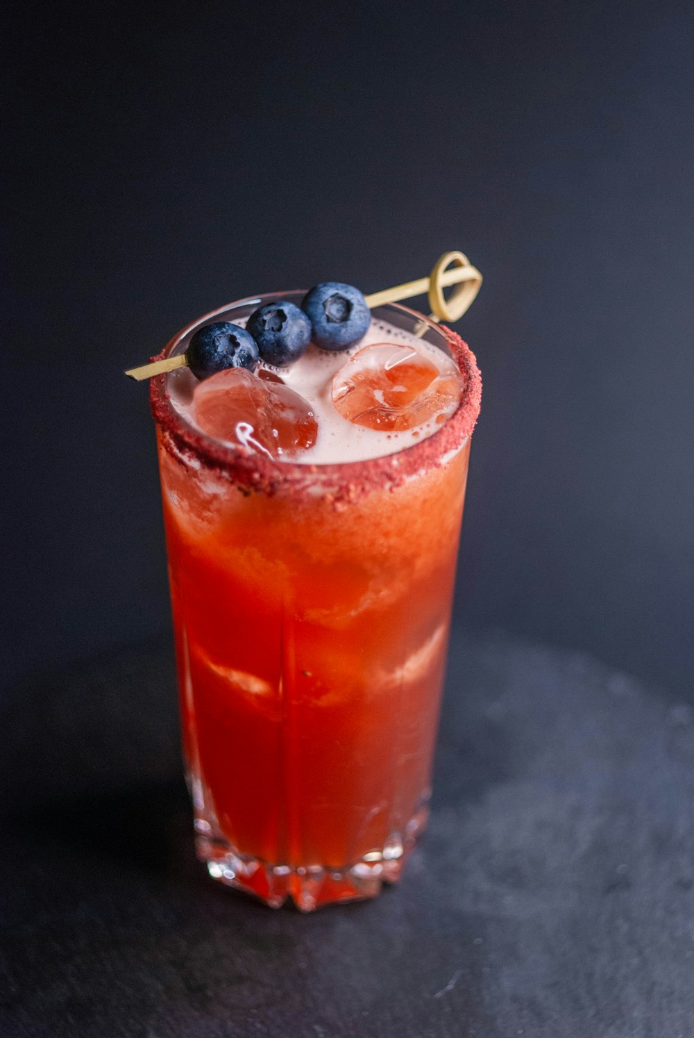 a red drink with blueberries and a gold garnish