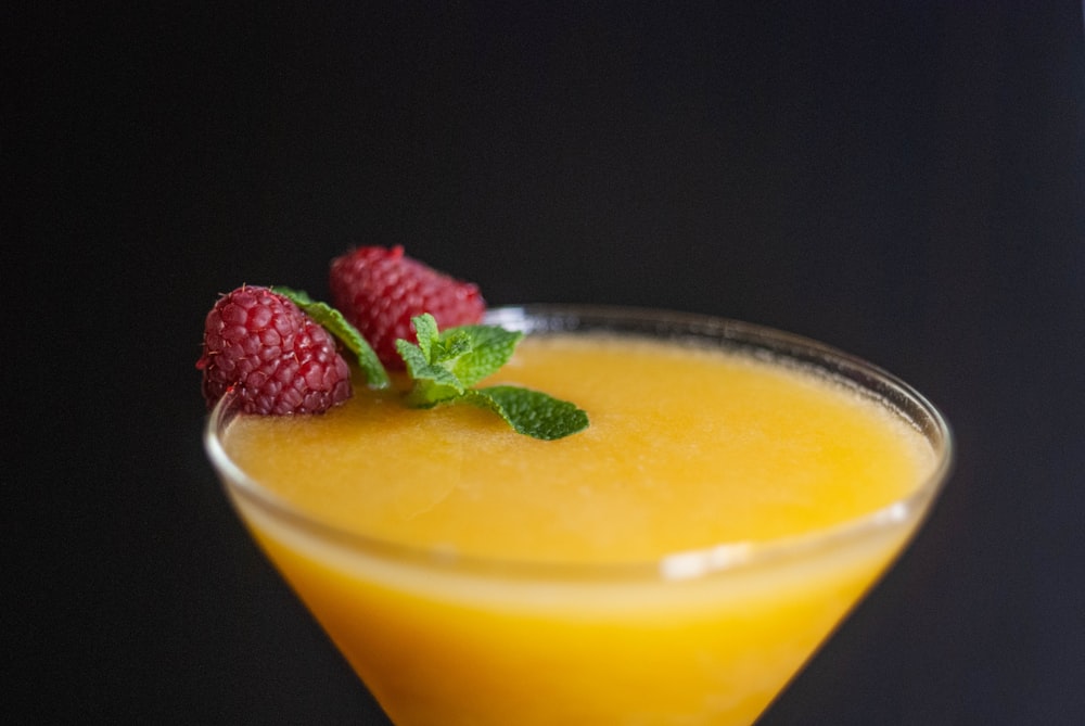 a close up of a drink in a glass with raspberries on the rim