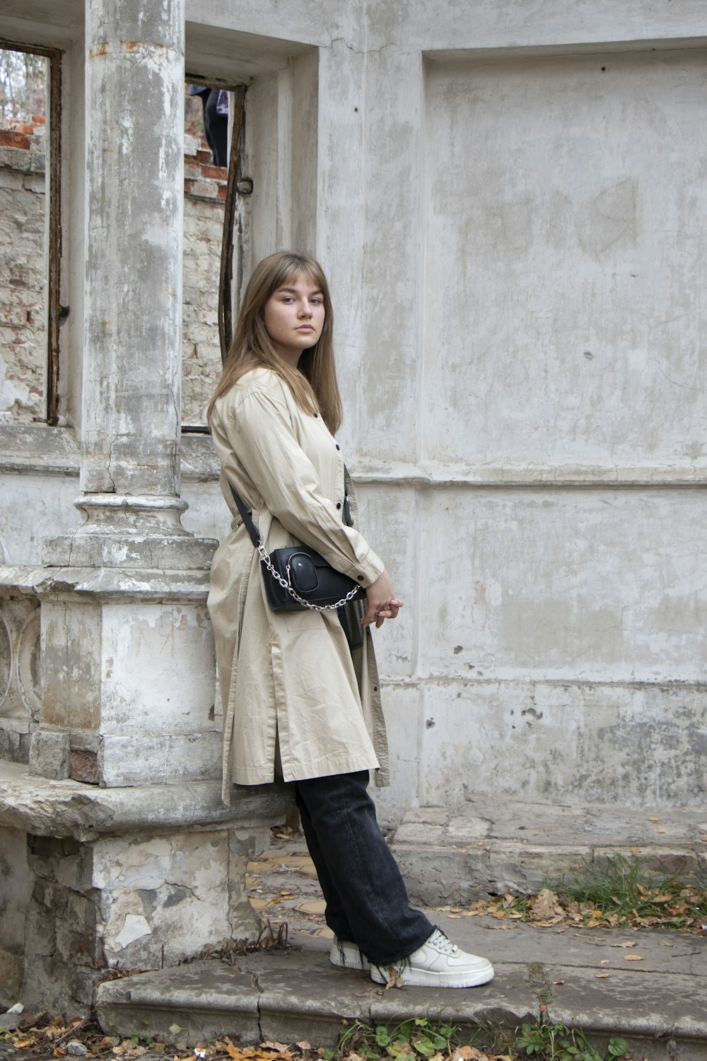 a woman leaning against a wall wearing a trench coat