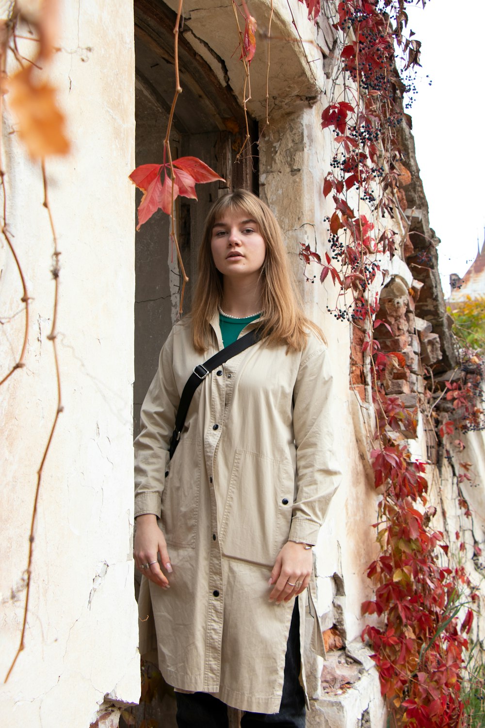 a woman in a trench coat leaning against a wall