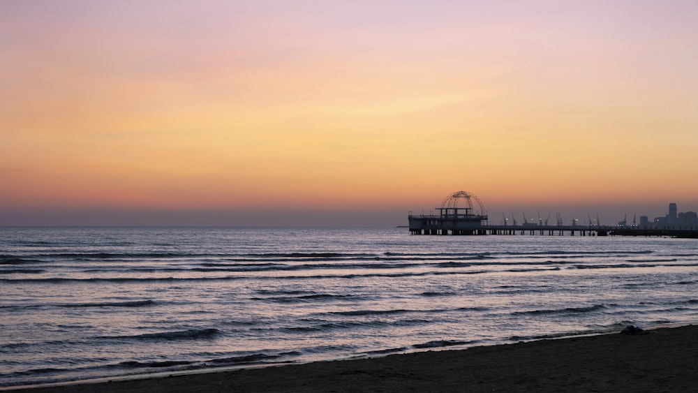 a sunset view of a beach with a pier in the distance