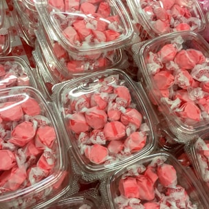 A collection of pink wrapped candies are neatly packed in clear plastic containers. Each candy is individually wrapped, showcasing a vivid pink color with bits of white from the wrappers. The containers are stacked closely together, creating a visually pleasing pattern of repeated shapes and colors.