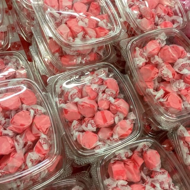A collection of pink wrapped candies are neatly packed in clear plastic containers. Each candy is individually wrapped, showcasing a vivid pink color with bits of white from the wrappers. The containers are stacked closely together, creating a visually pleasing pattern of repeated shapes and colors.