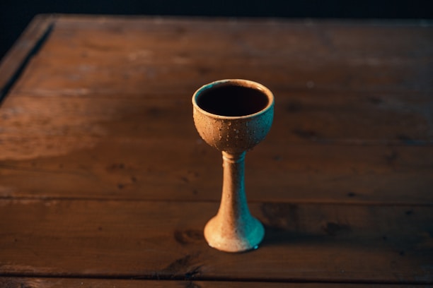 Close-up of a beautifully detailed silver kiddush cup catching soft light on a wooden table.