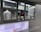 A person is working inside a street food or beverage kiosk, visible through a large service window. The kiosk has a menu in both English and another language, offering various items like teas, smoothies, and sandwiches. Inside, there are several kitchen equipment items and food supplies, suggesting a place for preparing orders.