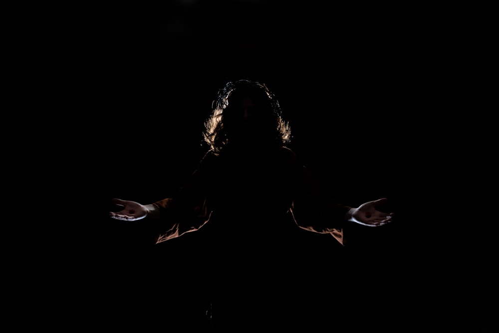 a woman standing in the dark with her arms outstretched