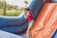 A child in a red shirt and green shorts is enjoying a water slide. The slide is inflatable with blue and orange colors, and water sprays are visible in the air. Lush greenery and palm trees are in the background, suggesting an outdoor setting.