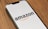 A smartphone displaying the Amazon logo against a plain background, positioned at an angle on a wooden surface.