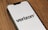 A smartphone lies on a wooden surface displaying the Verizon logo on its screen. The phone is positioned at an angle, showcasing the logo prominently against a white background.